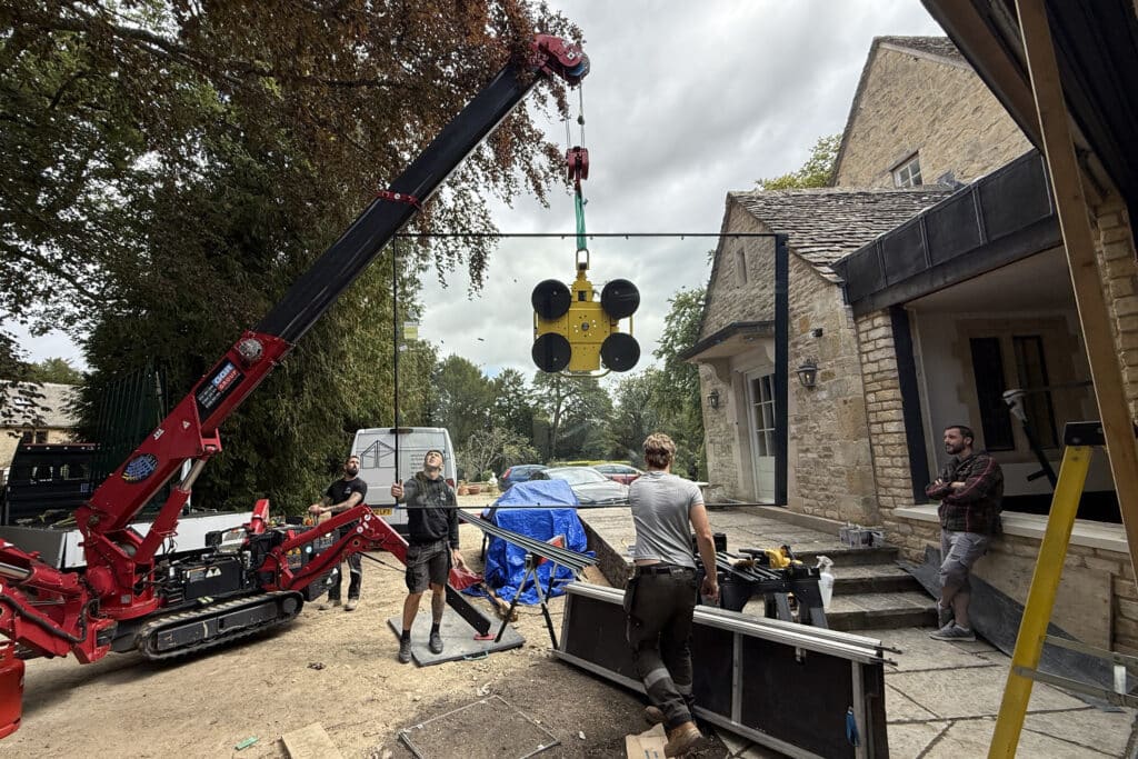 Mini spider crane lifting a 260kg frameless sliding door panel into place.