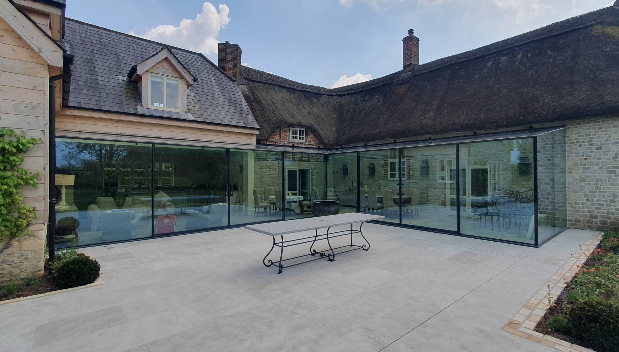 Exterior view of completed frameless glass extension blending with thatched cottage near Warminster 1