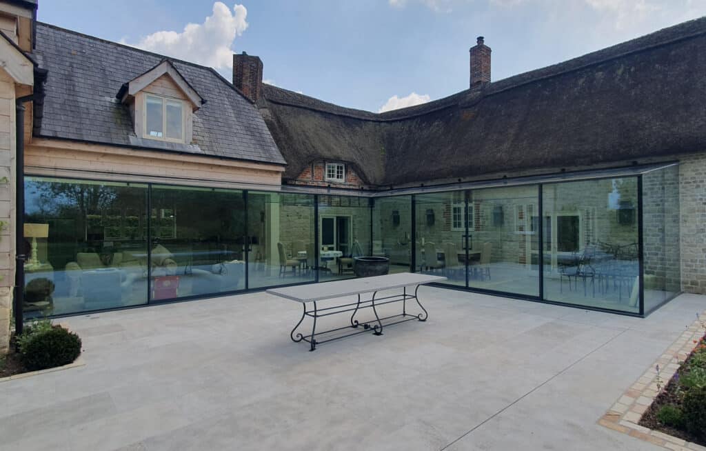 Exterior view of completed frameless glass extension blending with thatched cottage near Warminster