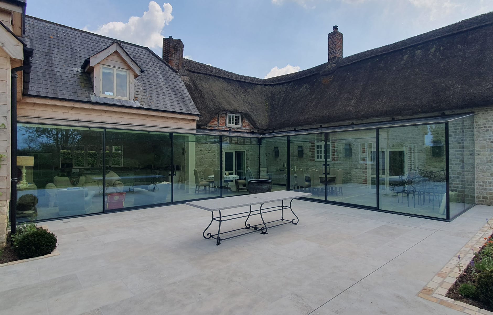 Exterior view of completed frameless glass extension blending with thatched cottage near Warminster