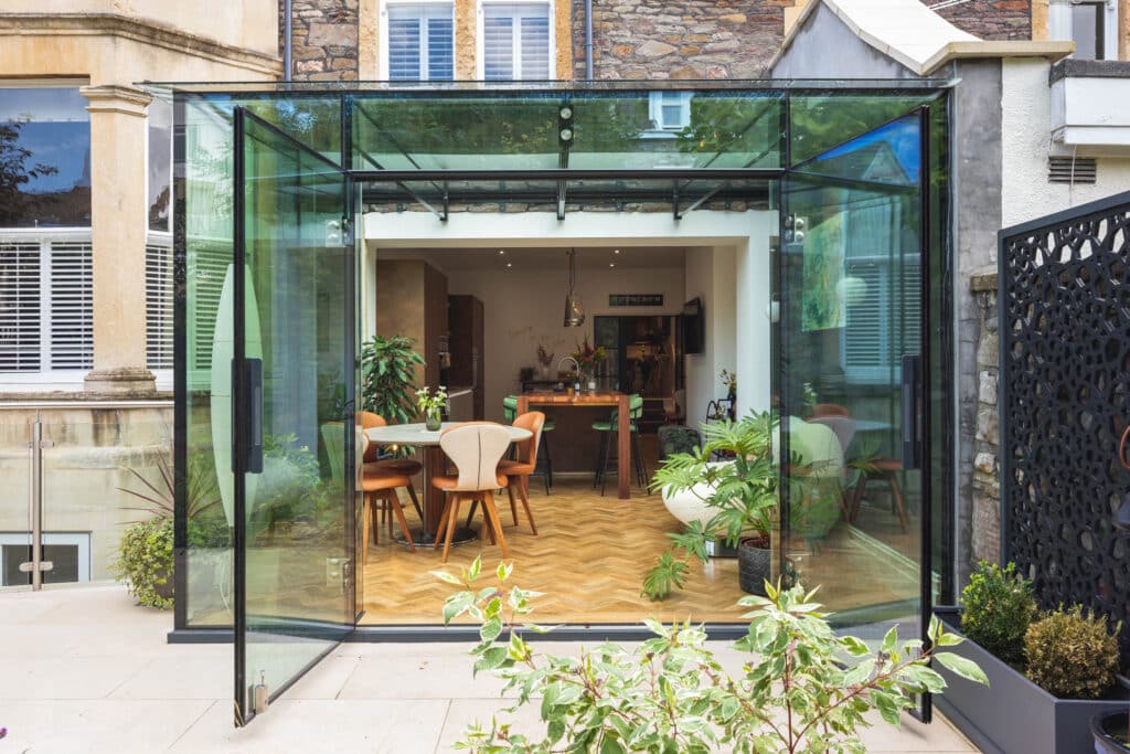 Completed glass kitchen extension viewed from garden in Bristol Alt text: External garden view of the finished glass kitchen extension in Bristol, showing the contemporary frameless design and bright living space.