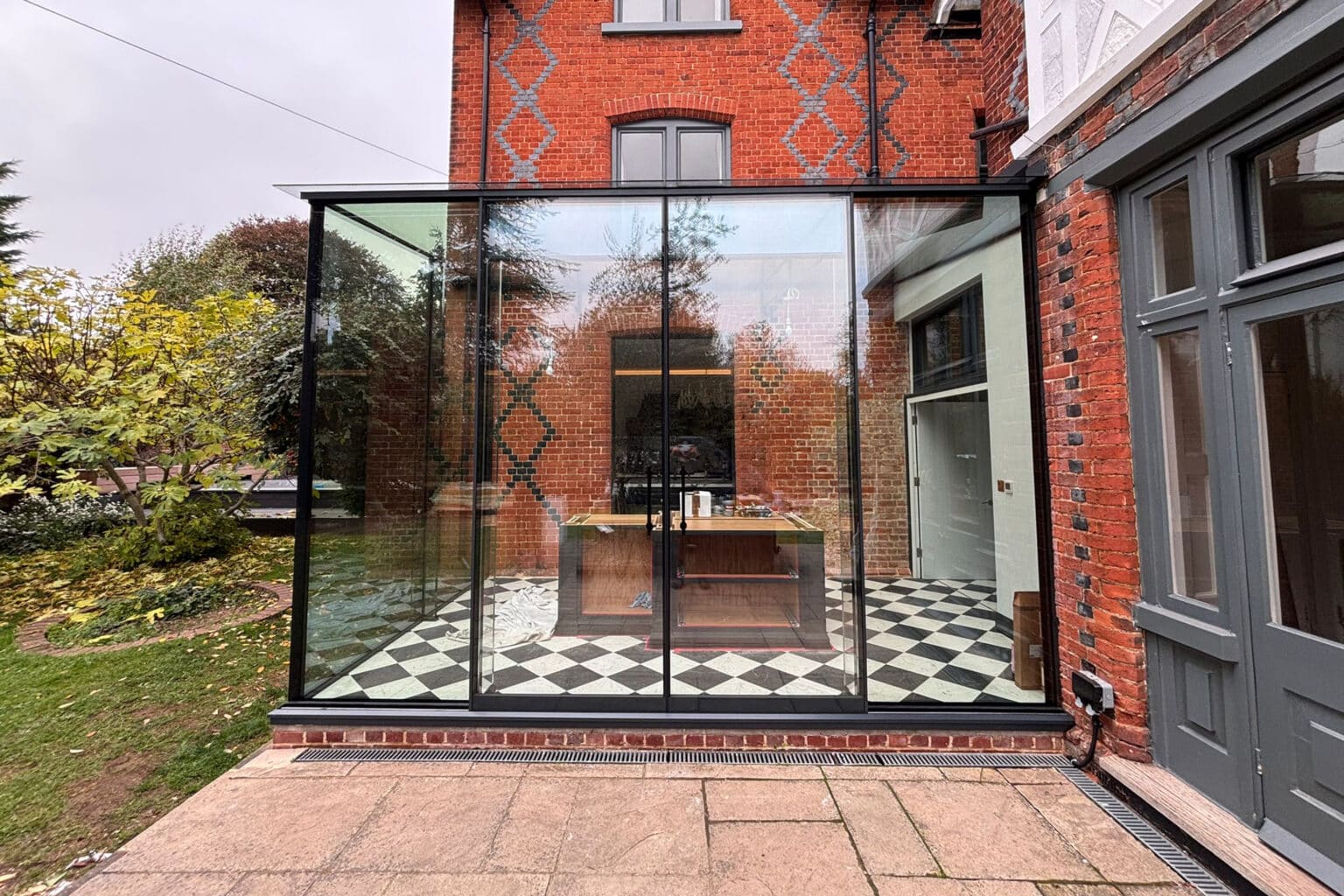 Completed structural glass extension with minimal-sightline sliding doors and frameless detailing.