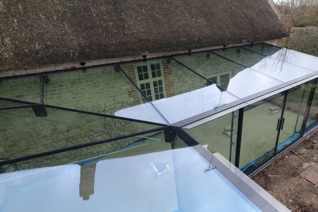 Close-up of frameless glass roof corner detail fitting beneath thatched roof.